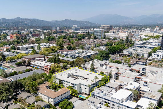 Aerial view of a city with various buildings and greenery, surrounded by distant mountains.