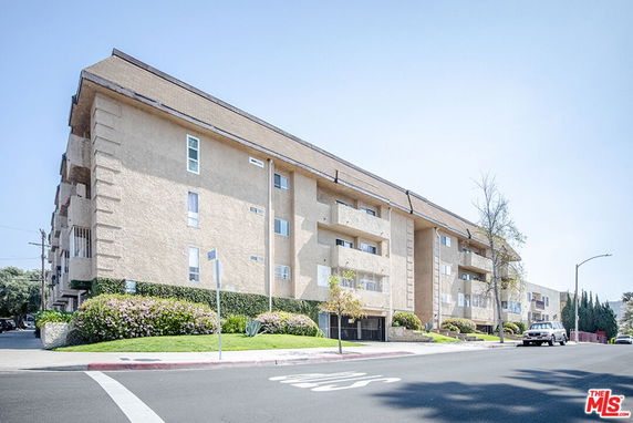 Front view of a multi-story apartment building with balconies and a sloped roof.