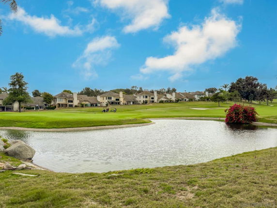 View of houses near a golf course with a small pond and green lawn under a blue sky.