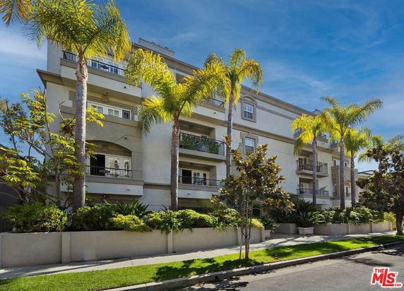 Front view of a multi-story residential building with balconies and palm trees.
