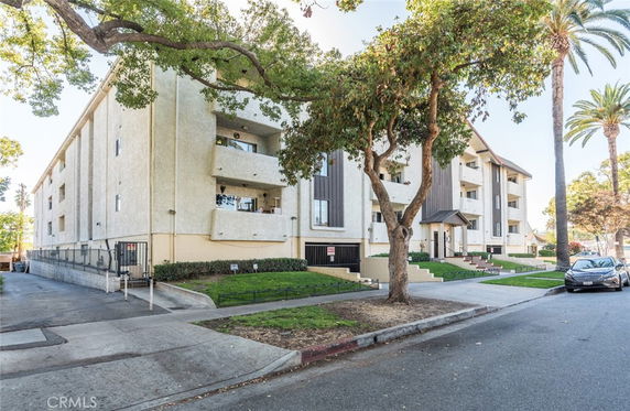 Front view of a multi-story apartment building with balconies and trees in front.