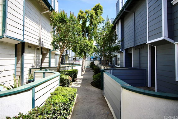 View of the front of townhouses with a pathway in between and small gardens.