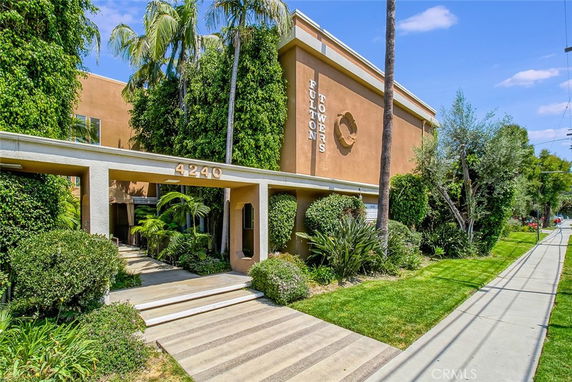Front view of a multi-story building with lush greenery and an entryway.