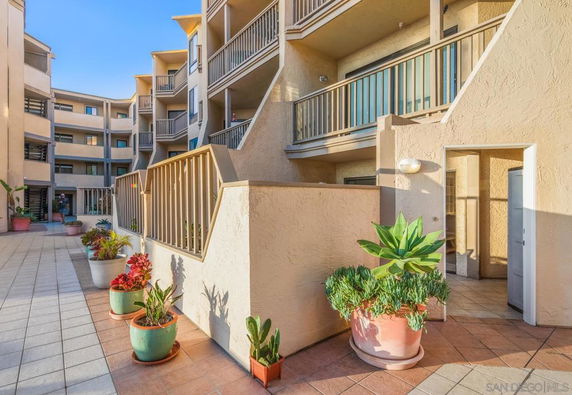 Front view of a multi-story building with balconies and potted plants.