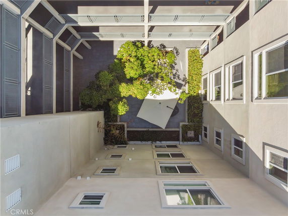 View of an internal courtyard surrounded by a multi-story building, featuring plants and a white umbrella.