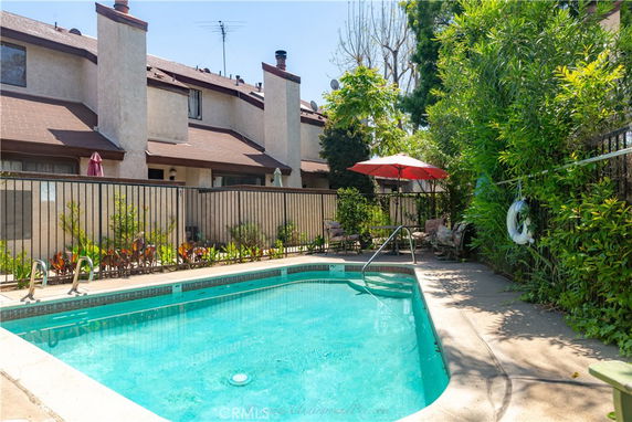 Outdoor swimming pool area with surrounding plants and buildings.