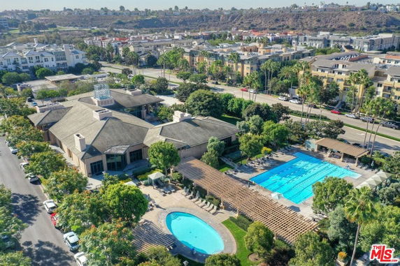 Aerial view of a large building complex with swimming pools surrounded by trees and residential buildings.