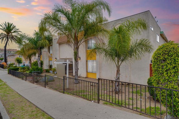 Front view of a two-story building with palm trees and a gated entrance.