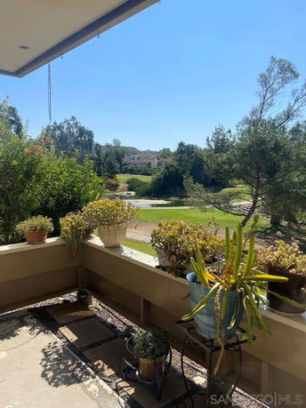 View from a balcony with potted plants overlooking a green landscape and distant buildings.
