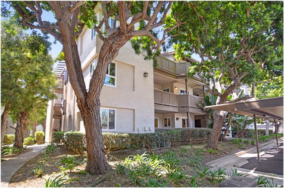 Front view of a multi-story residential building with balconies and windows, surrounded by trees.