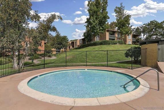 Outdoor circular swimming pool with metal fencing, located in a landscaped area with grass and trees.