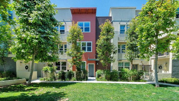 Front view of a multi-story residential building with balconies and trees in front.