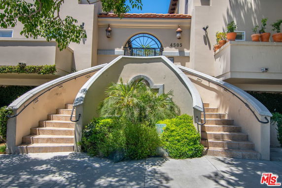 Front view of a multi-story building with symmetrical staircases and potted plants.