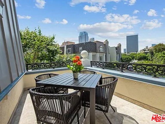 View from a rooftop patio with a table and chairs, surrounded by urban buildings and a clear sky.