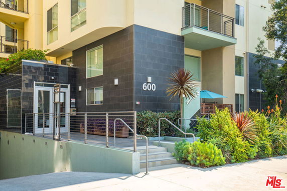 Front view of a modern multi-story building with balconies and a landscaped entrance.