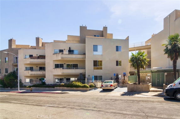 Front view of a multi-story apartment building with balconies and parking area.