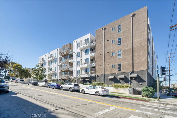 Front view of a multi-story apartment building with balconies and street parking.