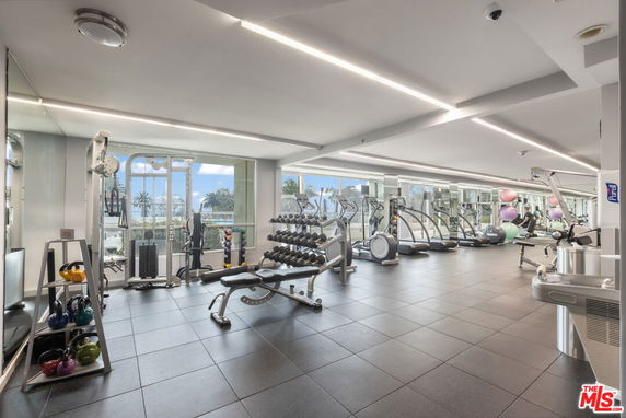 Indoor gym area with various exercise equipment and large windows.