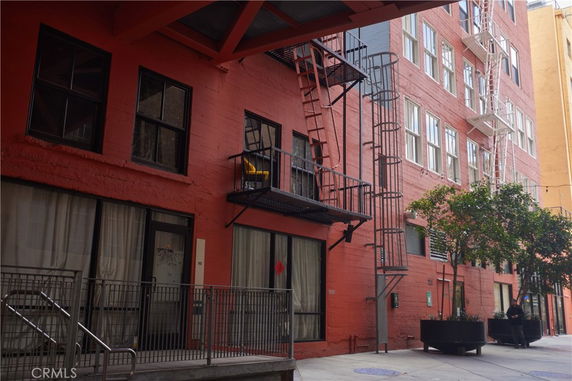 View of a multi-story red brick building with fire escape ladders and multiple windows.
