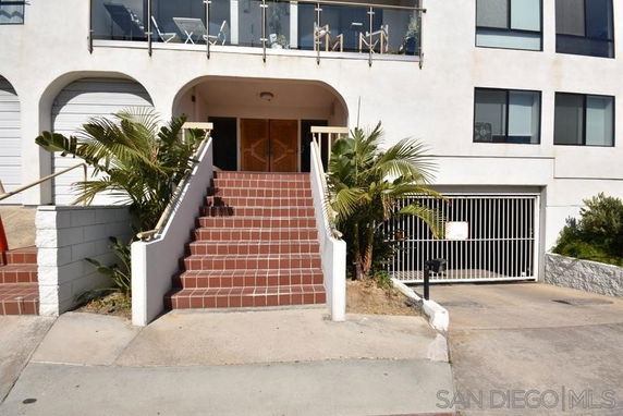 Front view of a multi-story building with stairs leading to the entrance and a balcony.