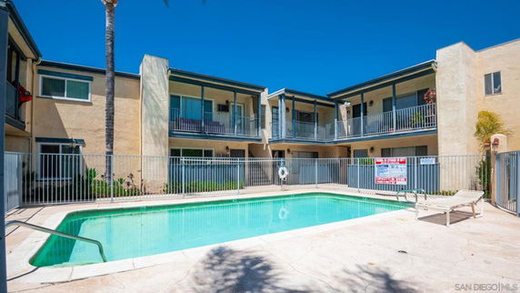 Two-story building complex with balconies overlooking a fenced swimming pool area.