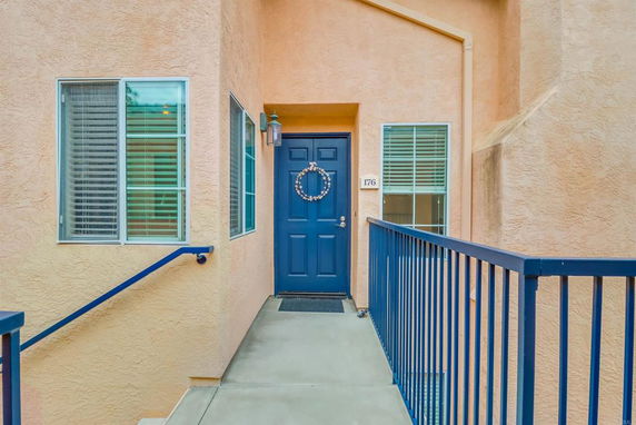 Front entrance of a house with a blue door and two windows on either side, accessible by a concrete ramp with blue railings.