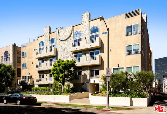 Front view of a multi-story apartment building with balconies and a stone facade.