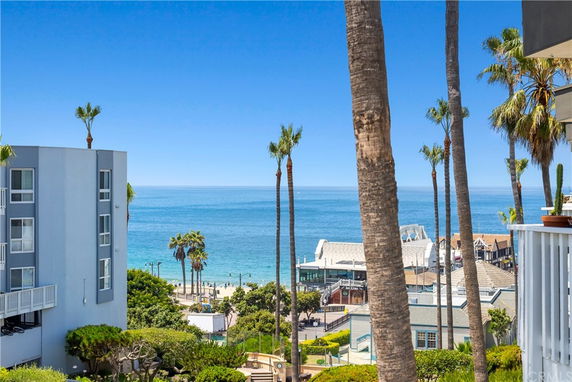 View of ocean and adjacent buildings from a higher vantage point, with palm trees in the foreground.