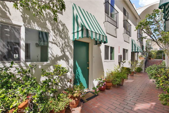 Front view of a building with green awnings and a walkway lined with potted plants.