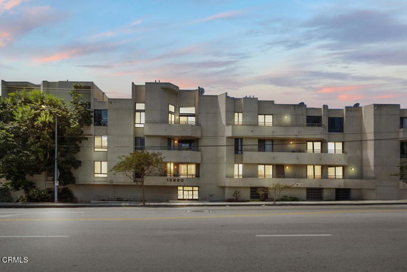 Front view of a multi-story apartment building with balconies and illuminated windows.