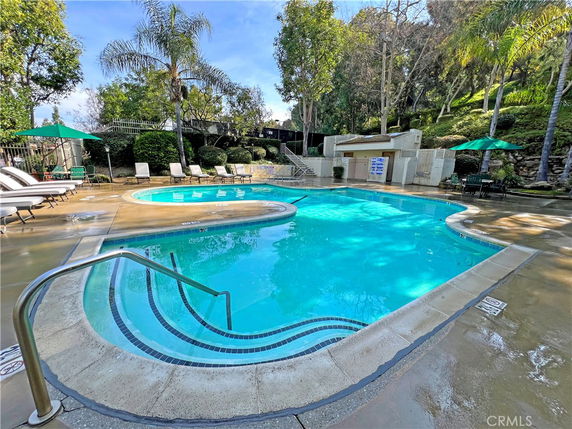 Outdoor swimming pool with surrounding lounge chairs and trees.