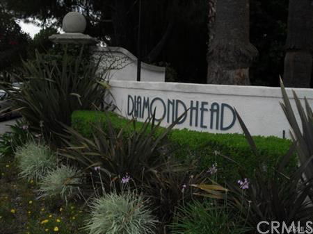 Front view of a sign labeled 'Diamond Head' on a white wall surrounded by plants.