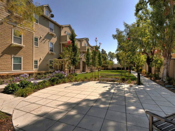 Exterior view of a multi-story residential building with pathway and benches in foreground.