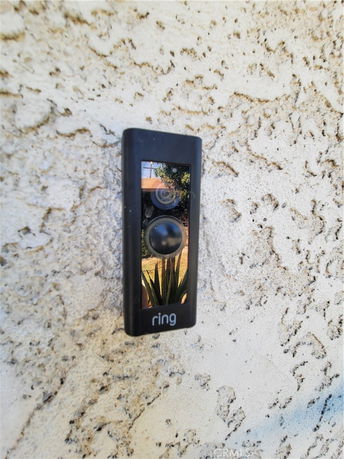 Close-up of a wall-mounted video doorbell on a textured exterior surface.