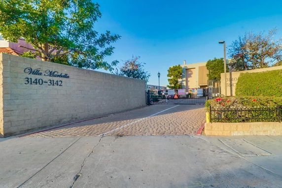 Front view of a building entrance with a gated driveway and sign 'Villa Marbella 3140-3142'.