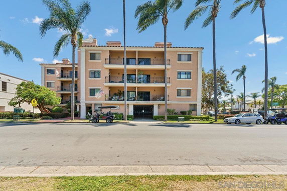 Front view of a multi-story apartment building with balconies and palm trees.