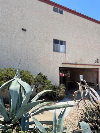 Front view of a building with large plants in front and a covered parking area.
