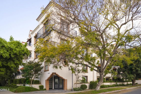 Front view of a multi-story building with balconies and surrounded by trees.