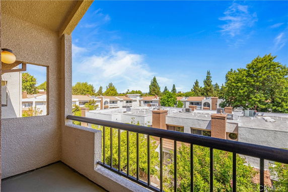 Balcony view overlooking residential rooftops with surrounding trees.