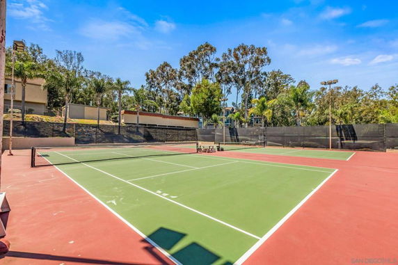 Outdoor tennis court with surrounding trees and buildings.