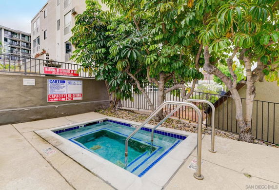 Small outdoor swimming pool area with a railing and trees nearby.
