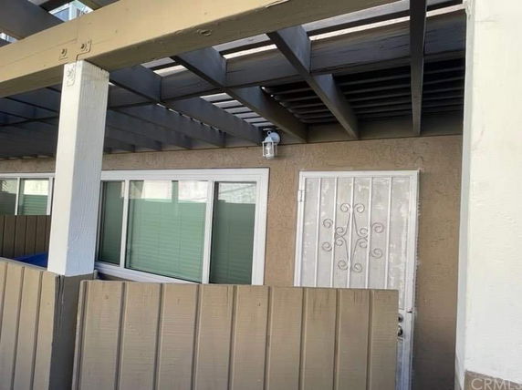 Exterior view of a house with a decorative metal door and large window under a wooden pergola.