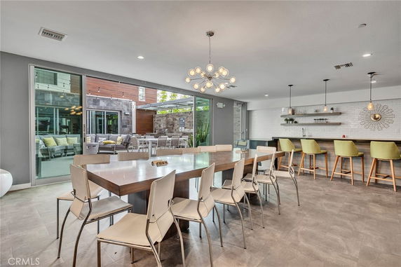 Interior view of a clubhouse with a large dining table and chairs, a bar counter with stools, and sliding glass doors leading outside.