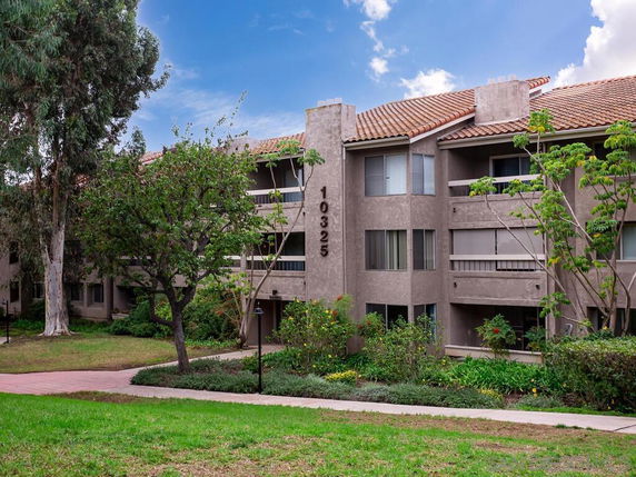 Front view of a multi-story apartment building with balconies and a tiled roof.