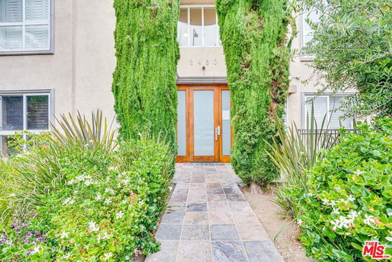 Front view of a building entrance with glass doors and tall greenery.
