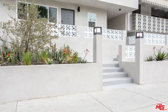 Front view of a modern two-story building with decorative concrete railings and a small landscaped garden.