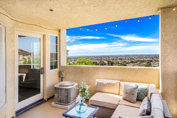 Outdoor seating area on a balcony with a view of the cityscape in the distance.