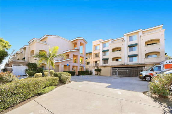 Front view of a multi-story apartment building with balconies and a parking area.