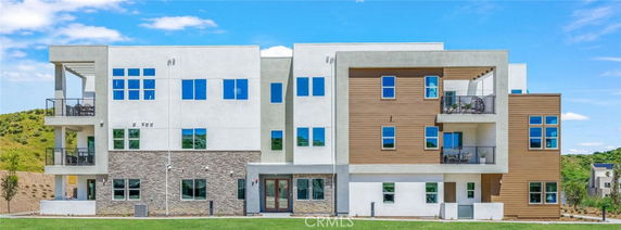 Front view of a modern multi-story building with a mix of materials including stone, wood, and glass.