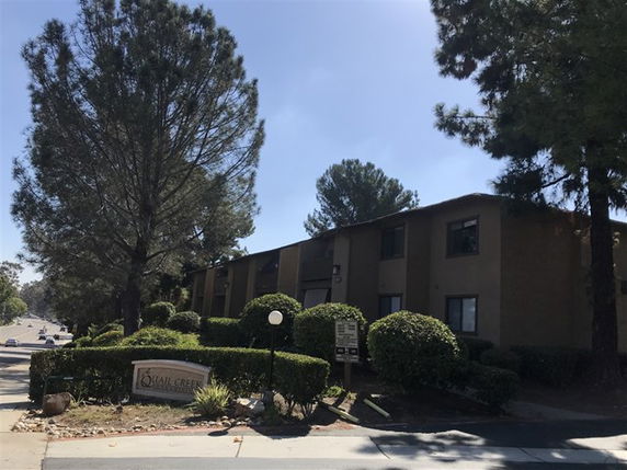 Front view of a multi-story residential building with trees and hedges.